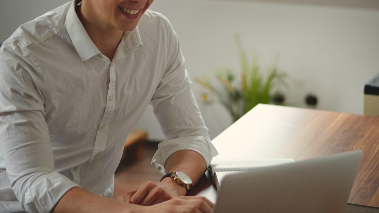 Mitarbeiter arbeitet lächelnd am Laptop im modernen Büro
