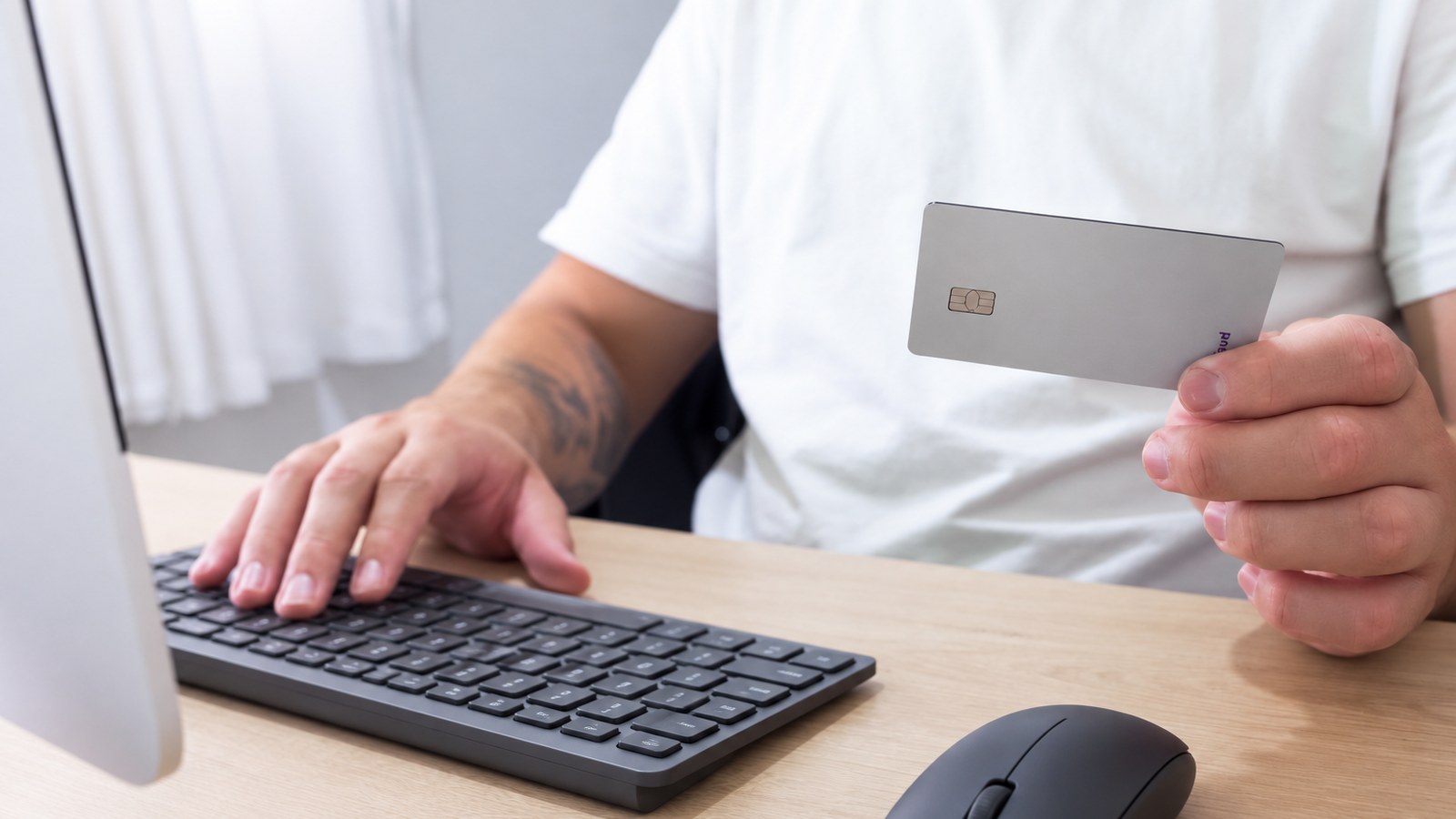 Person haelt eine Zahlungskarte in der Hand waehrend sie am Computer eine digitale Zahlung vorbereitet